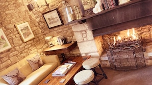 A cozy room with a stone wall, a fireplace, a sofa, a wooden table, and two stools. - Inn For All Seasons (Burford)