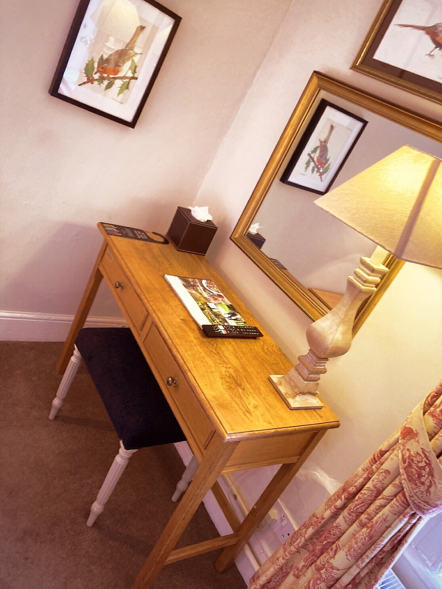 A wooden desk with a remote control, a tissue box, and a magazine. A mirror and a lamp are on the wall.