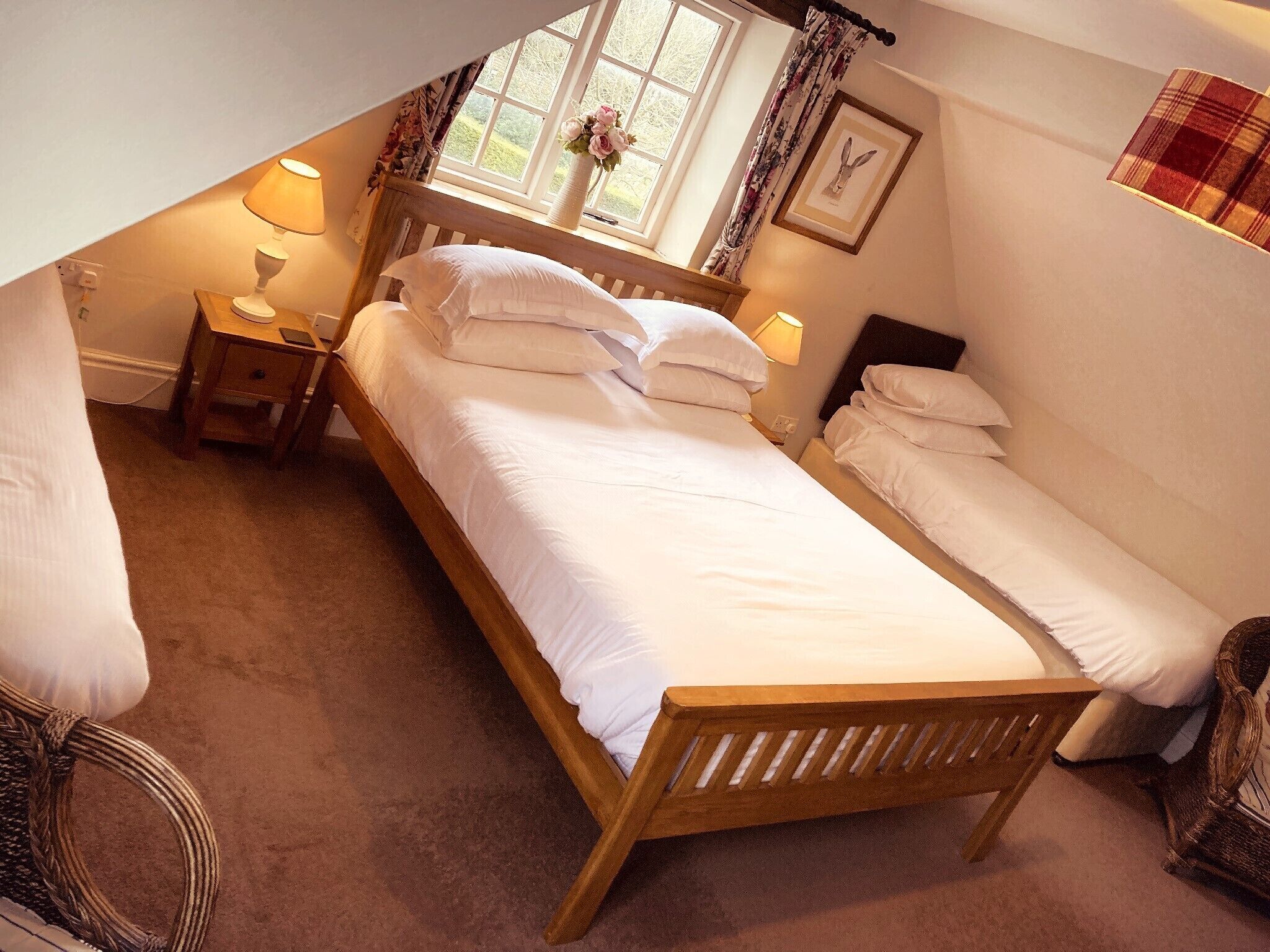 Un dormitorio acogedor con una cama de madera, dos mesitas de noche con lámparas, una ventana con cortinas florales y un cuadro en la pared.