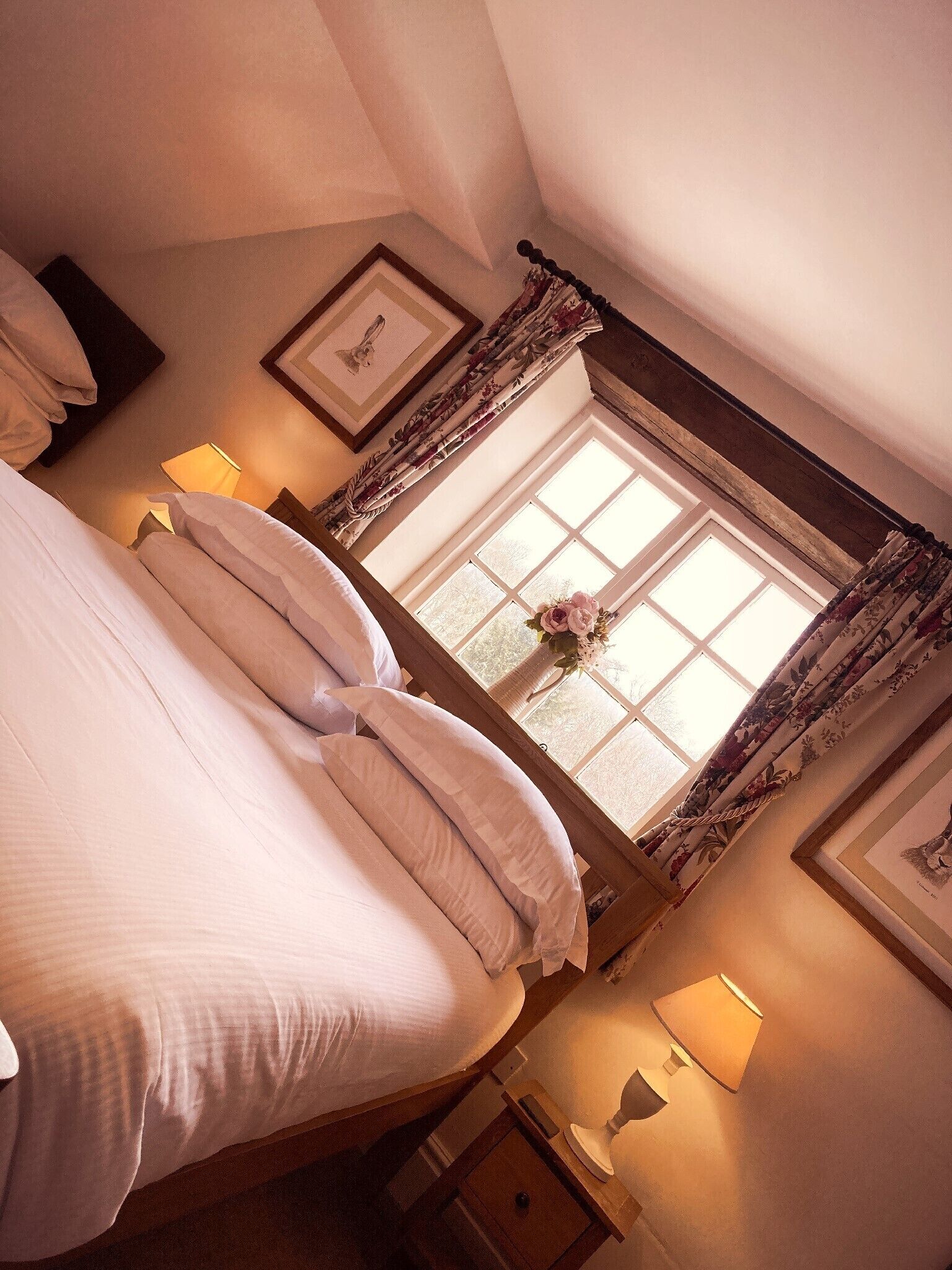A bedroom with a large bed, a window with floral curtains, and a bedside lamp.