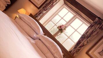 A bedroom with a large bed, a window with floral curtains, and a bedside lamp.