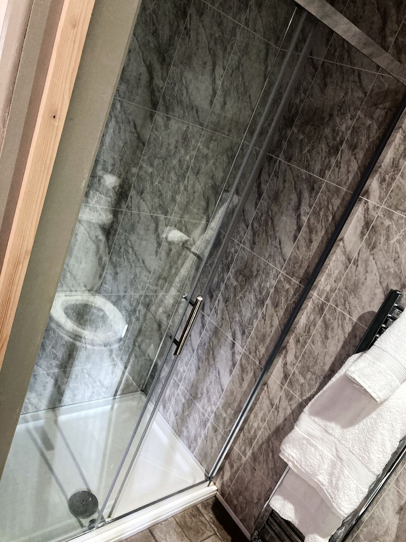 A glass-enclosed shower with a marble wall.