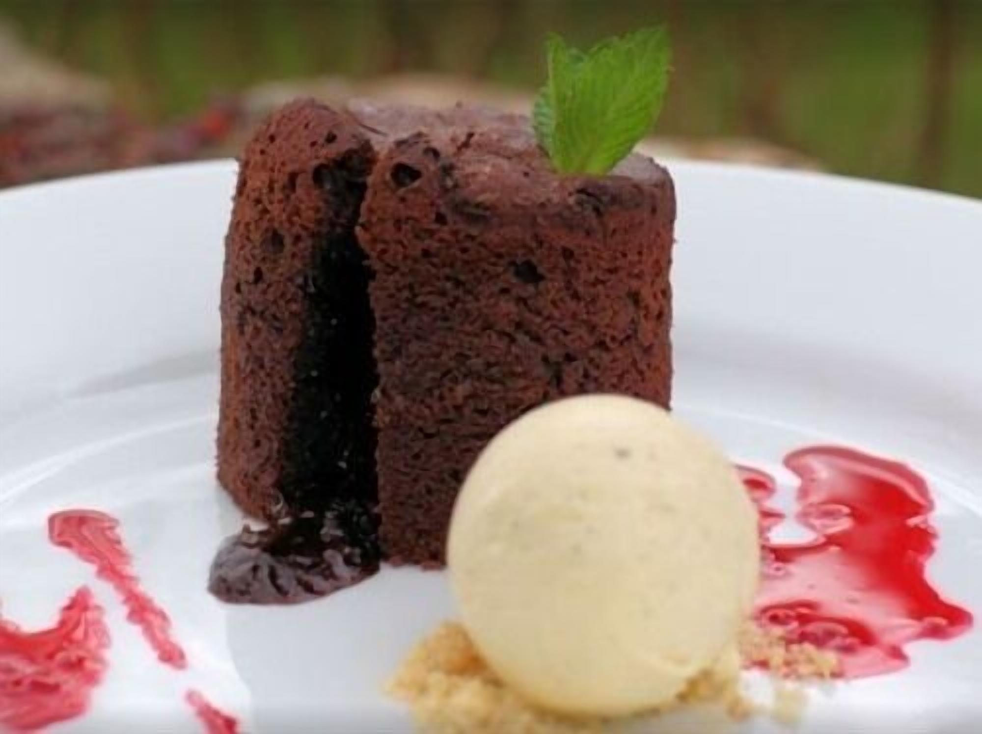 Dessert met chocolade lava cake, een bolletje vanille-ijs en een muntblaadje op een wit bord.