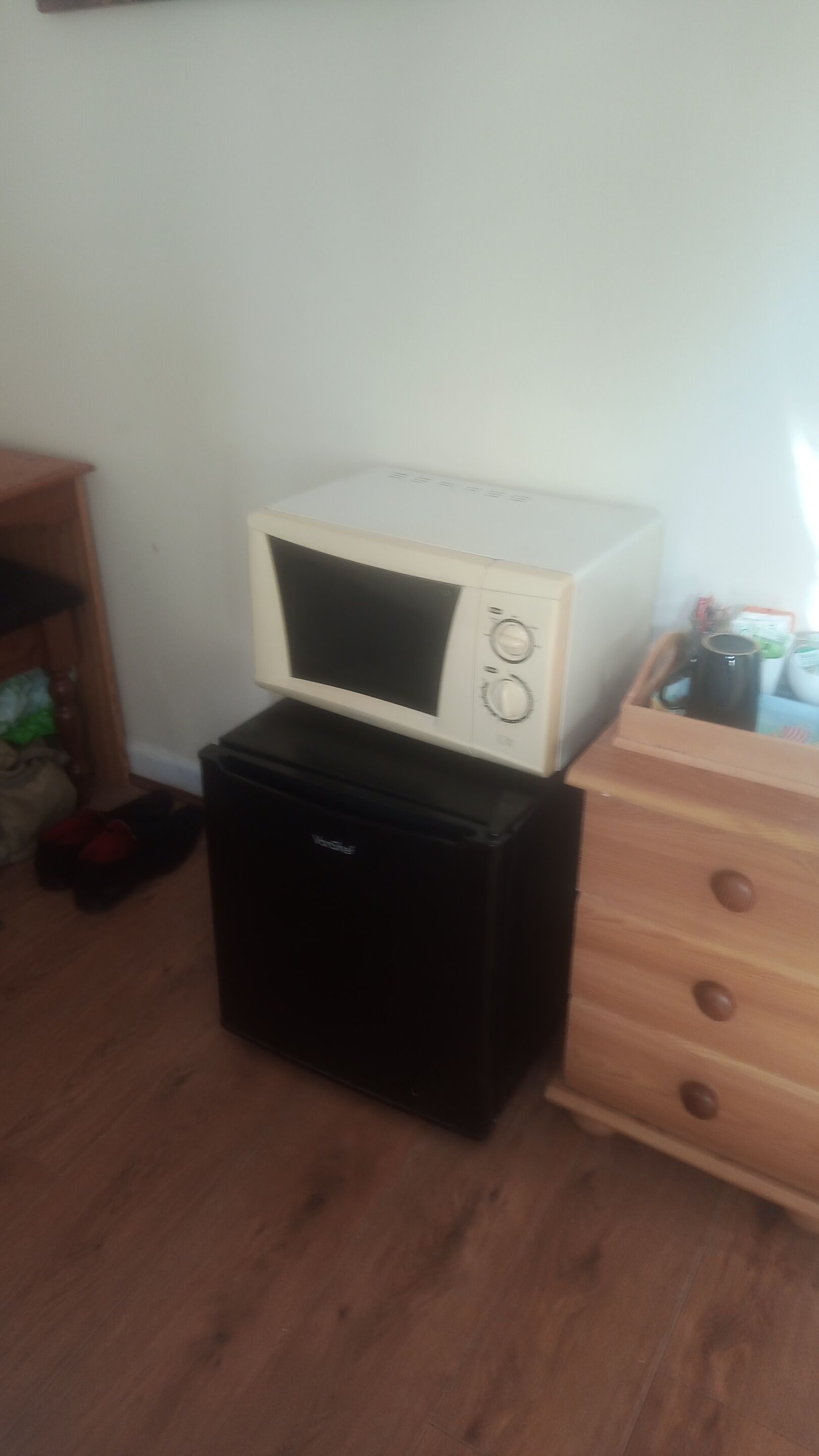 A white microwave on a black appliance, a wooden dresser, and a wooden cabinet.