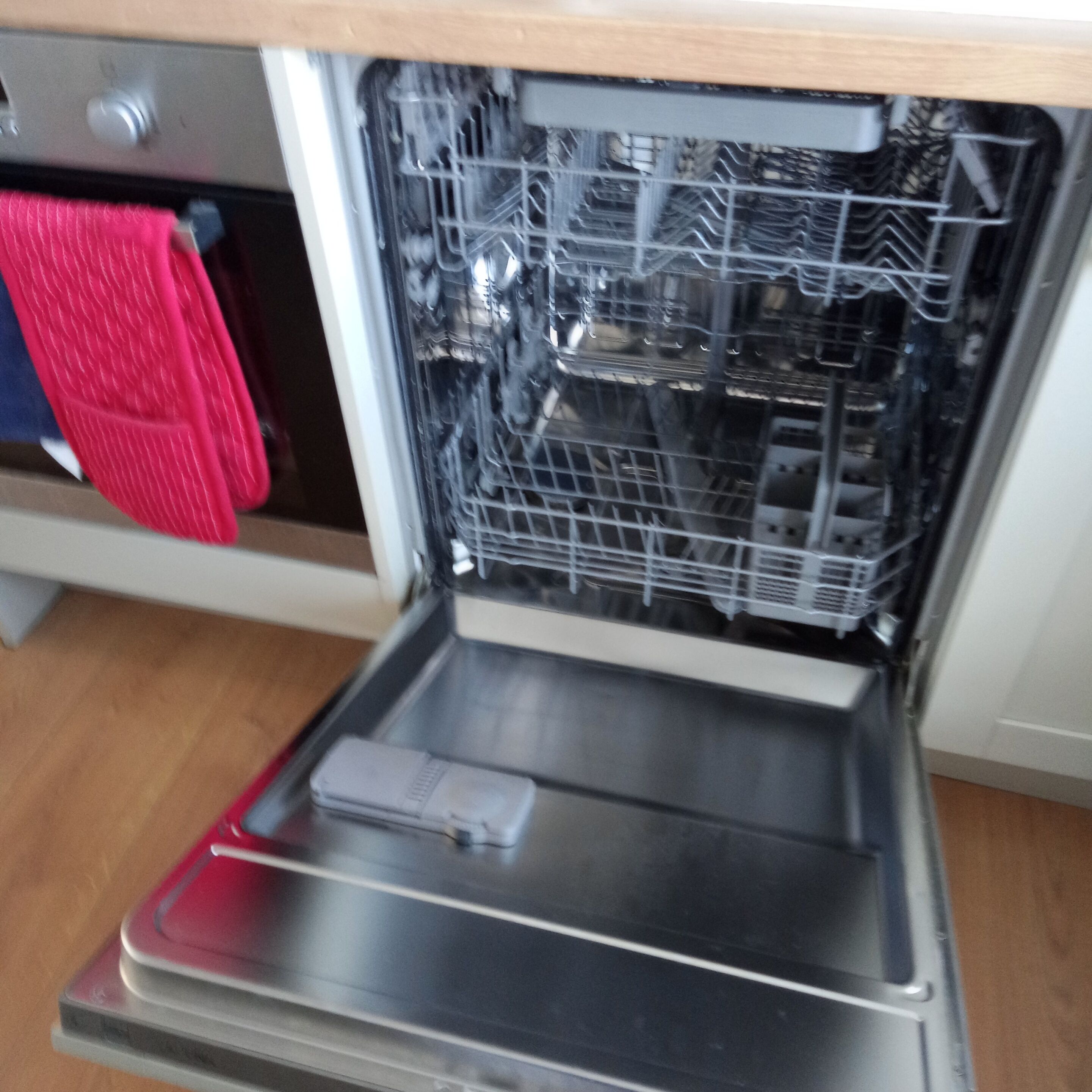 An open dishwasher with a red towel hanging nearby.