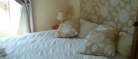 A bed with white bedding and floral-patterned headboard, a bedside lamp, and a window with curtains.