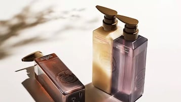 Tres botellas de champú, acondicionador y jabón de baño sobre una superficie reflectante.