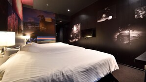Hotellihuone, jossa on suuri sänky, yöpöytä, seinälle asennettu televisio ja suuri juliste seinällä.
