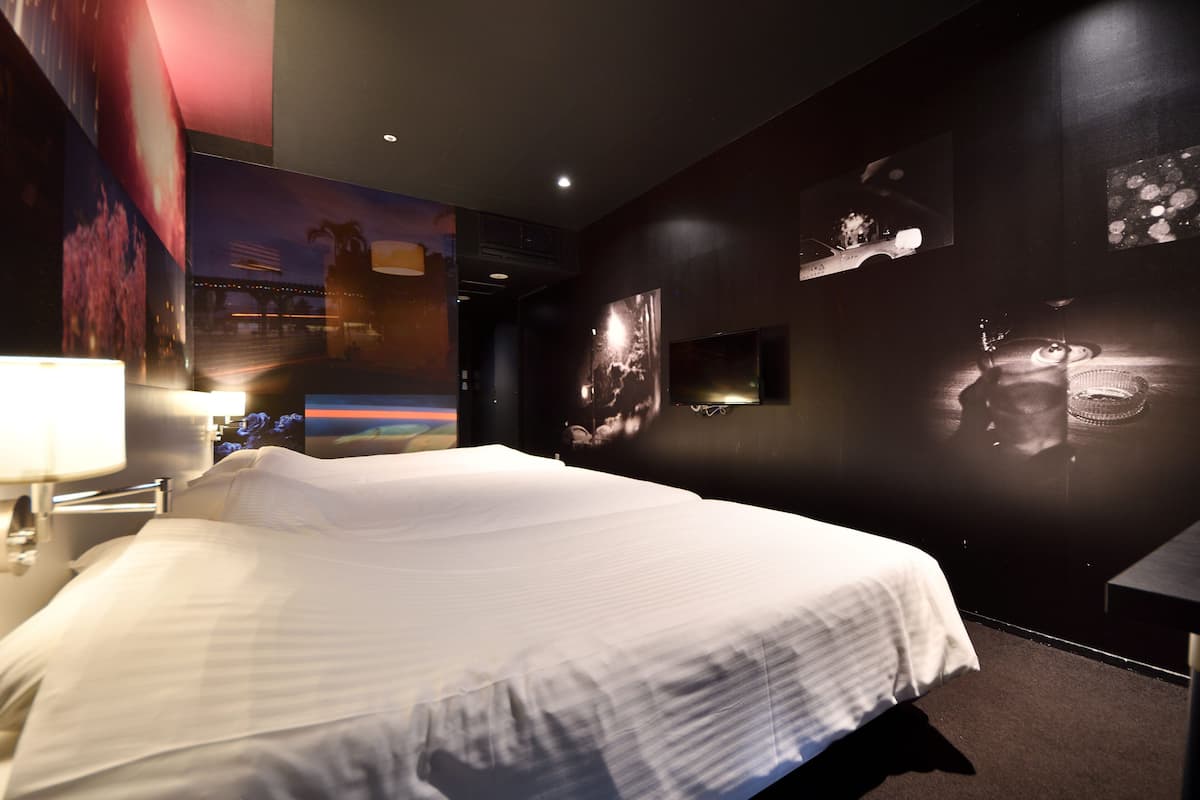 Une chambre d’hôtel avec un grand lit, une table de chevet, un téléviseur fixé au mur et une grande affiche accrochée au mur.