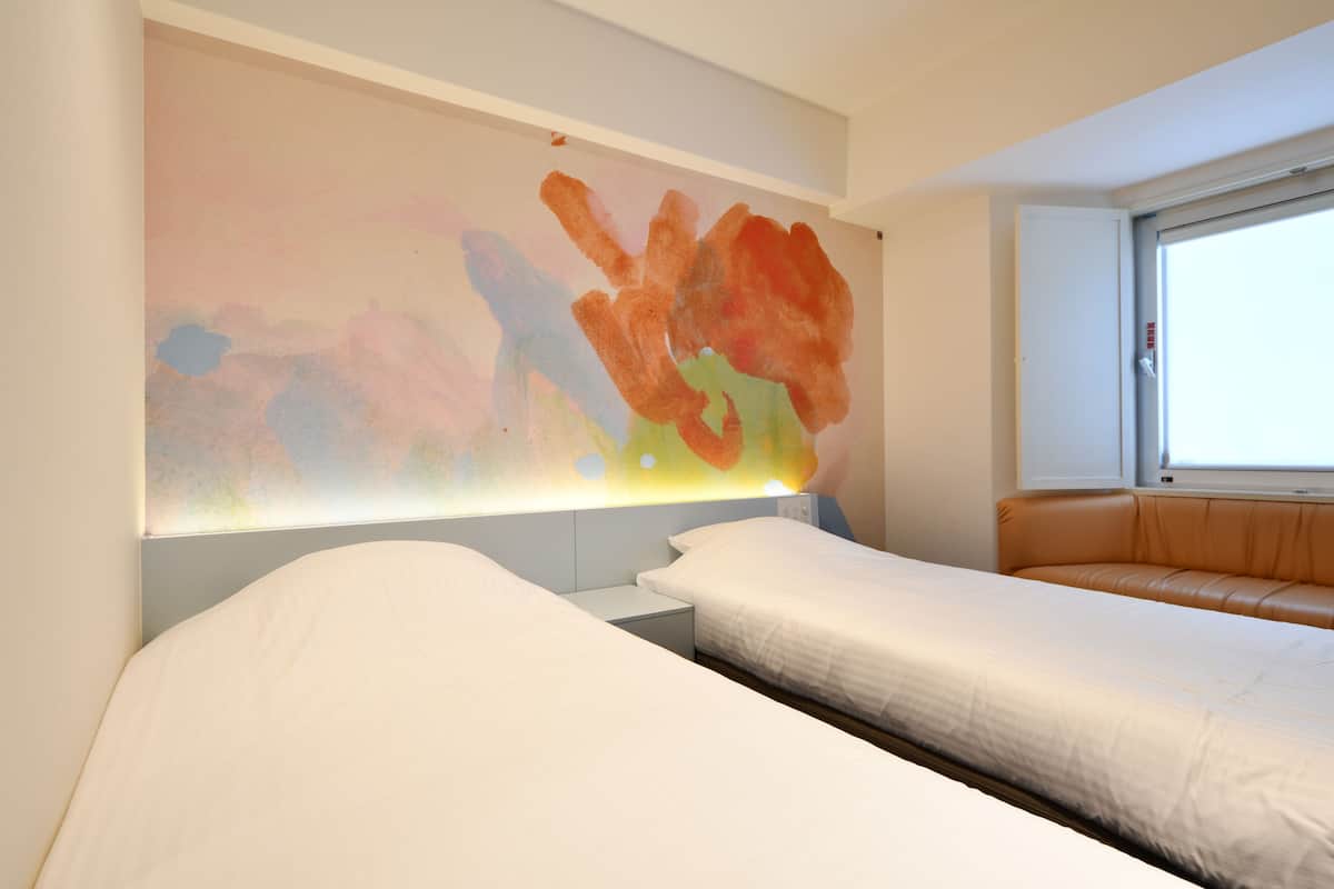 Une chambre d’hôtel avec deux lits, une grande peinture abstraite au mur et une fenêtre donnant sur l’extérieur.