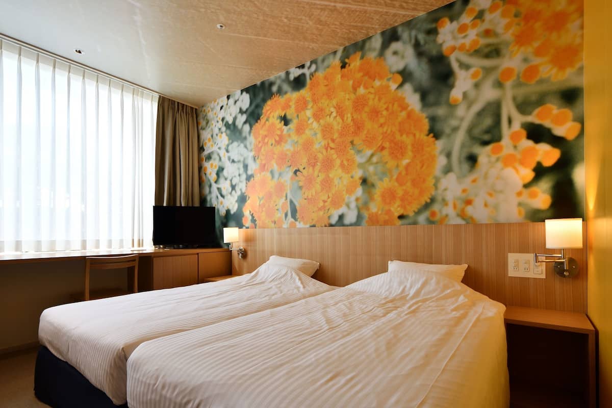Une chambre d’hôtel avec deux lits, un téléviseur posé sur un bureau et une décoration murale à motifs floraux.