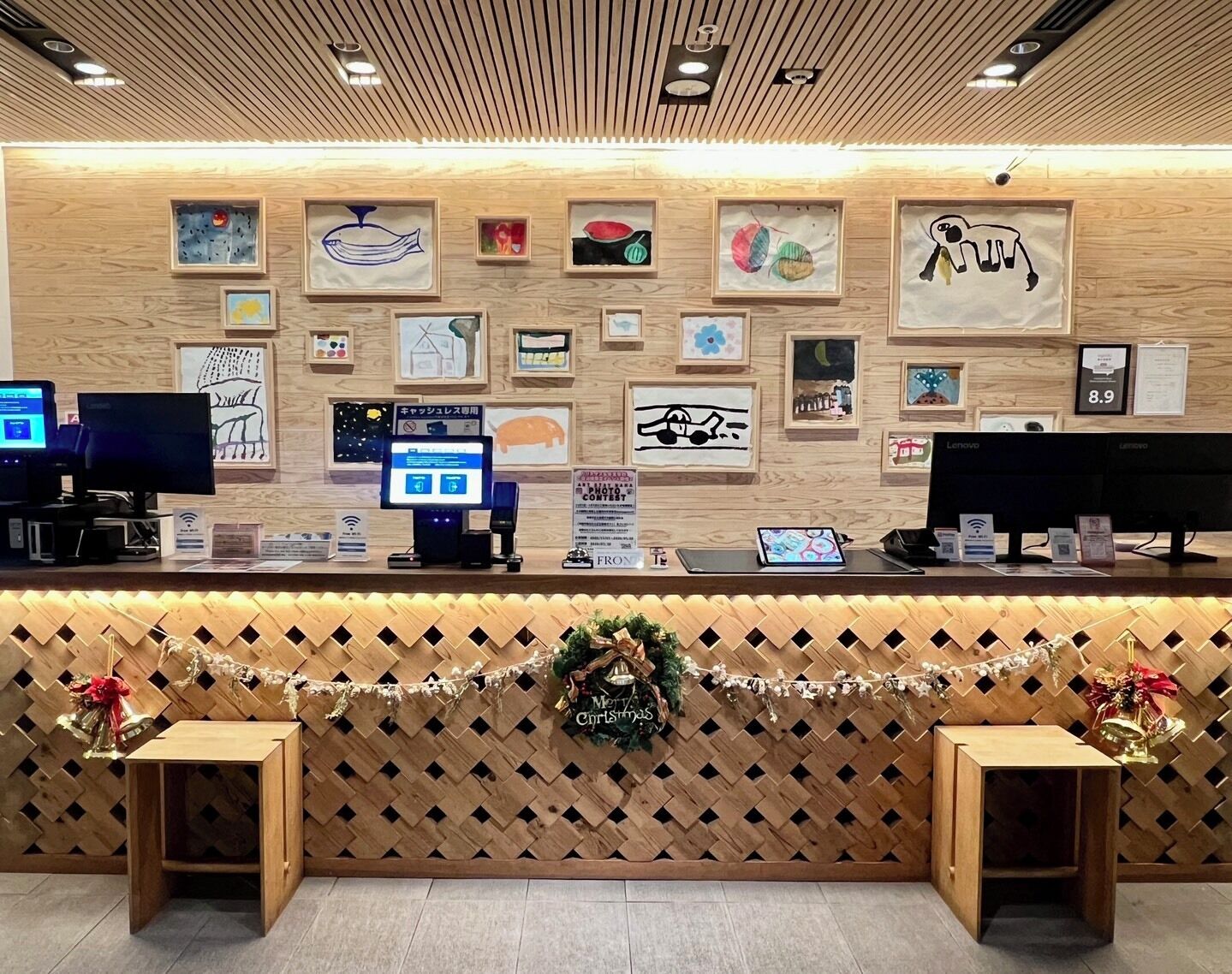 A reception desk with framed artwork, a digital kiosk, and a Christmas wreath.