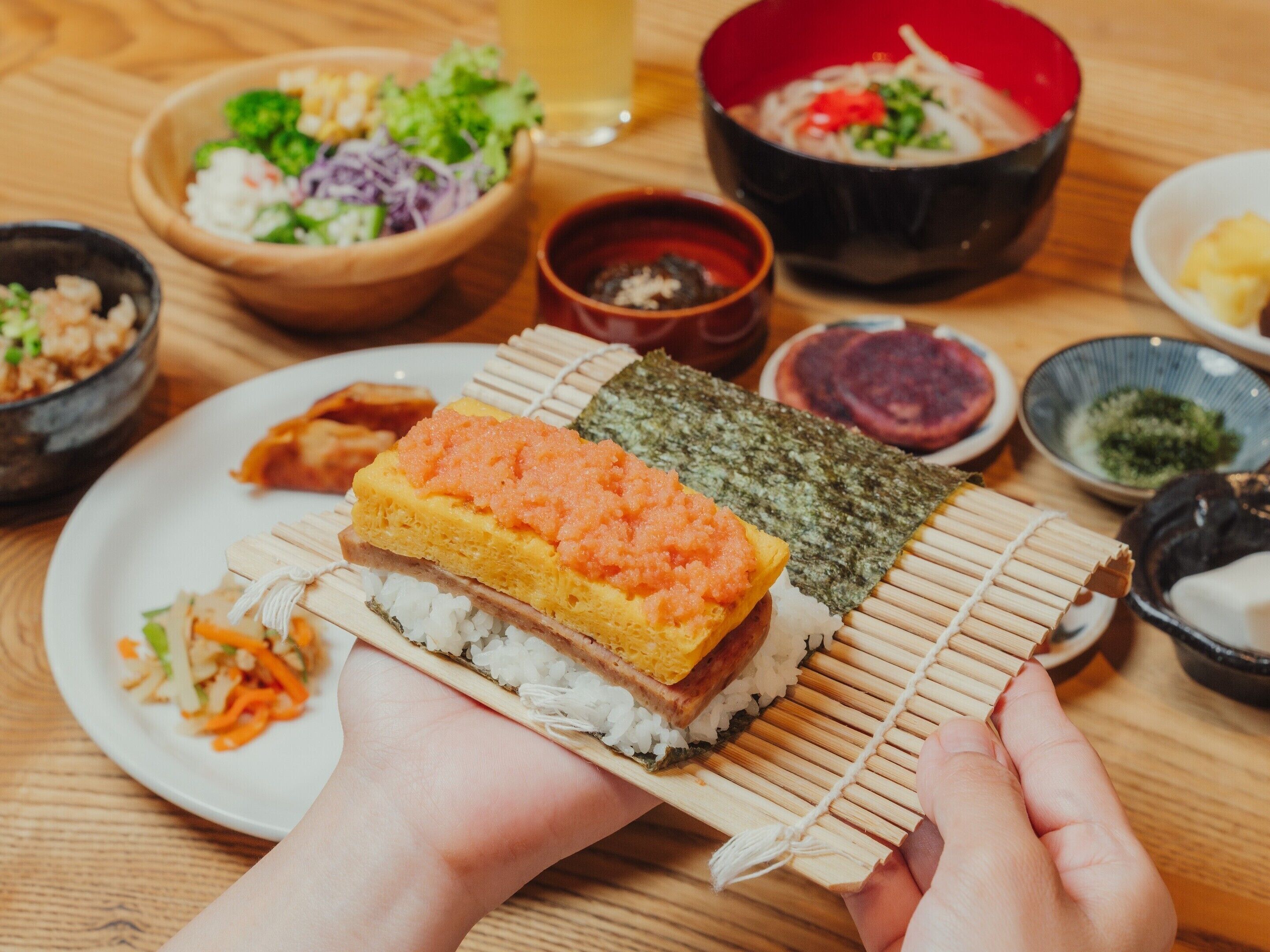 A sushi dish with a wooden presentation board, surrounded by various side dishes and condiments on a wooden table.