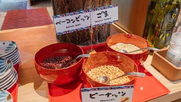 A buffet table with labeled bowls of bacon bits, sesame seeds, and peanuts.