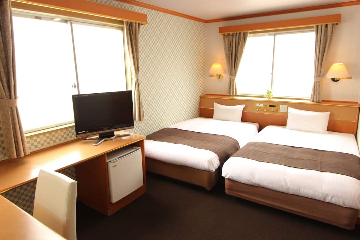 A hotel room with two beds, a desk with a television, and a small refrigerator.