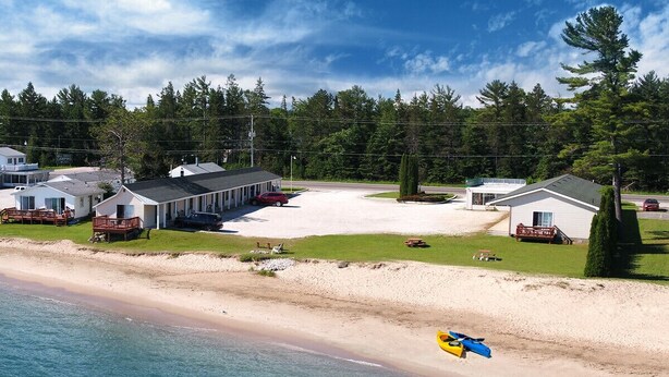 A coastal hotel with multiple buildings, a sandy beach, and a kayak. - Northwinds Motel (Mackinaw City)