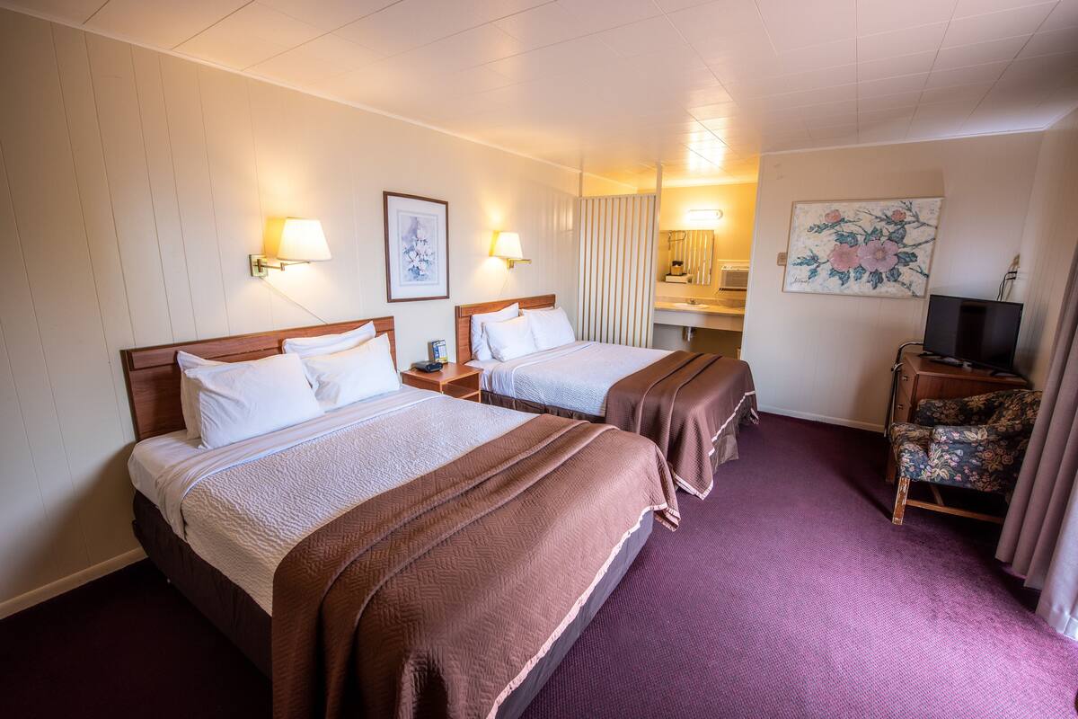 A hotel room with two beds, a television, a mirror, and a painting on the wall.