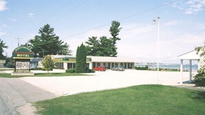 A motel with a beach sign, a parking lot, and a view of the ocean. - Northwinds Motel (Mackinaw City)