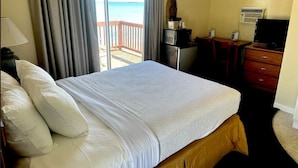 A hotel room with a bed, a desk, a television, and a view of the ocean. - Northwinds Motel (Mackinaw City)