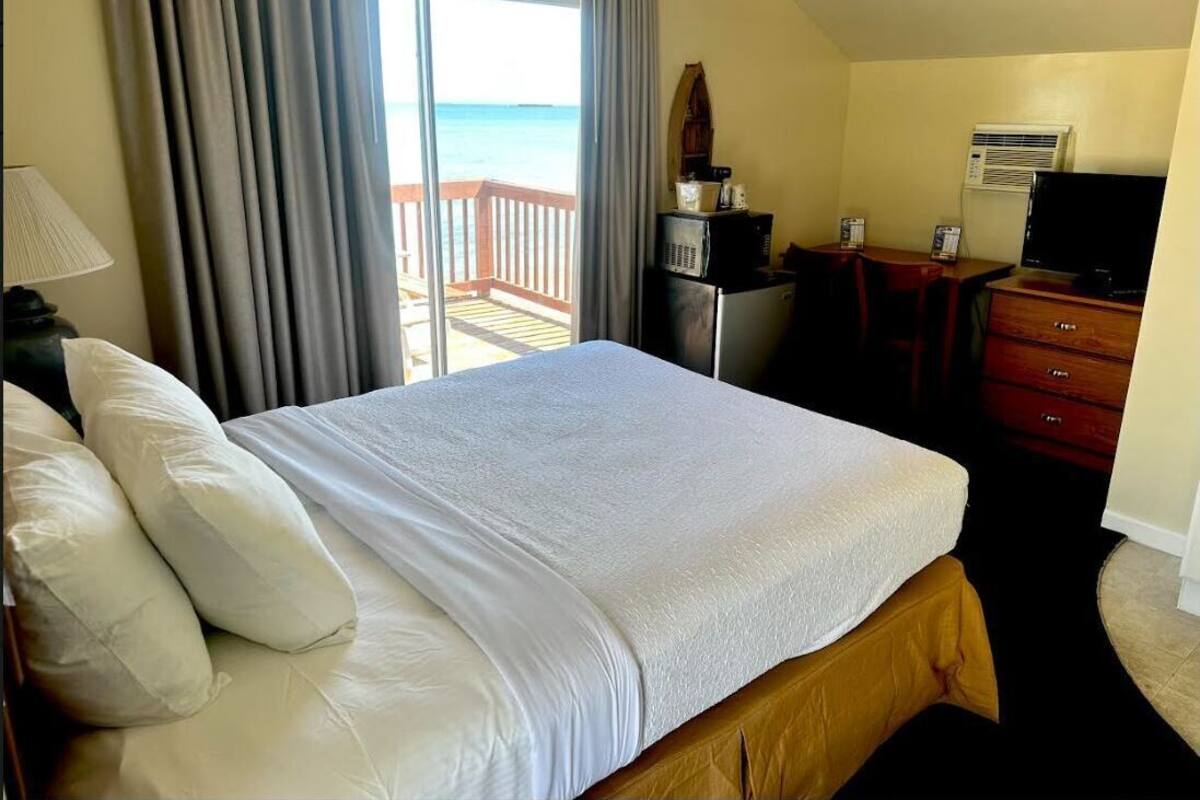 A hotel room with a bed, a desk, a television, and a view of the ocean.