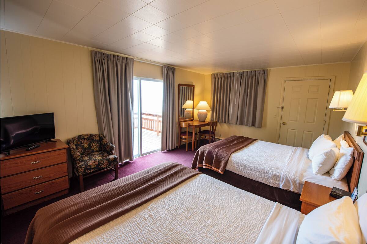 A hotel room with two beds, a television, a desk, and a chair.