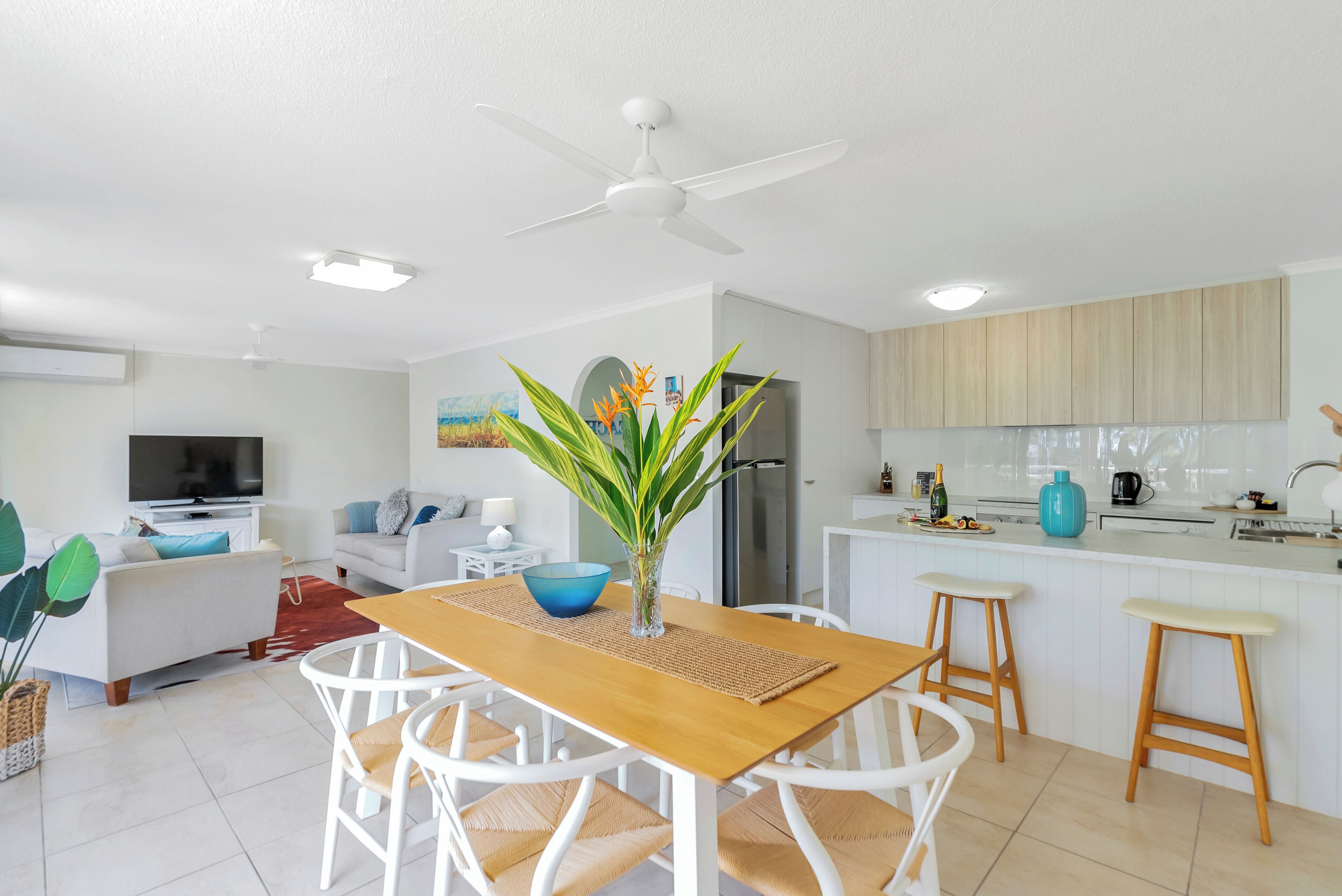 A modern kitchen with white cabinetry, a wooden dining table, and a ceiling fan.