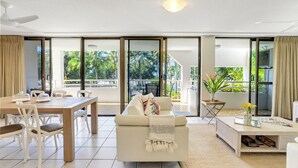 Una sala de estar moderna con un sofá, una mesa de comedor y sillas. Hay un vidrio corredero que da a un balcón con vistas a zonas verdes.