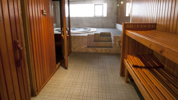 A sauna room with wooden benches, a hot tub, and a tiled floor.