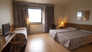 A hotel room with a bed, two bedside tables, a desk with a chair, a television, and a window with curtains.