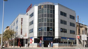 A modern hotel with a prominent 'HOTEL DOMO' sign, a 'la Sirena' restaurant, and a clear blue sky.