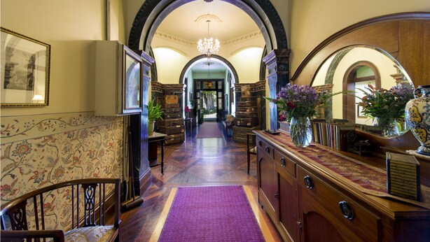 A grand hallway with a purple carpet, wooden furniture, and floral wallpaper.