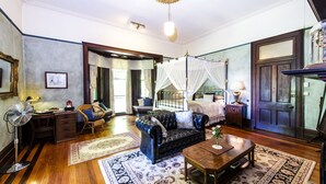 A room with a leather sofa, wooden coffee table, and a bed with a canopy. There is a fan, a lamp, and a picture frame on the wall.