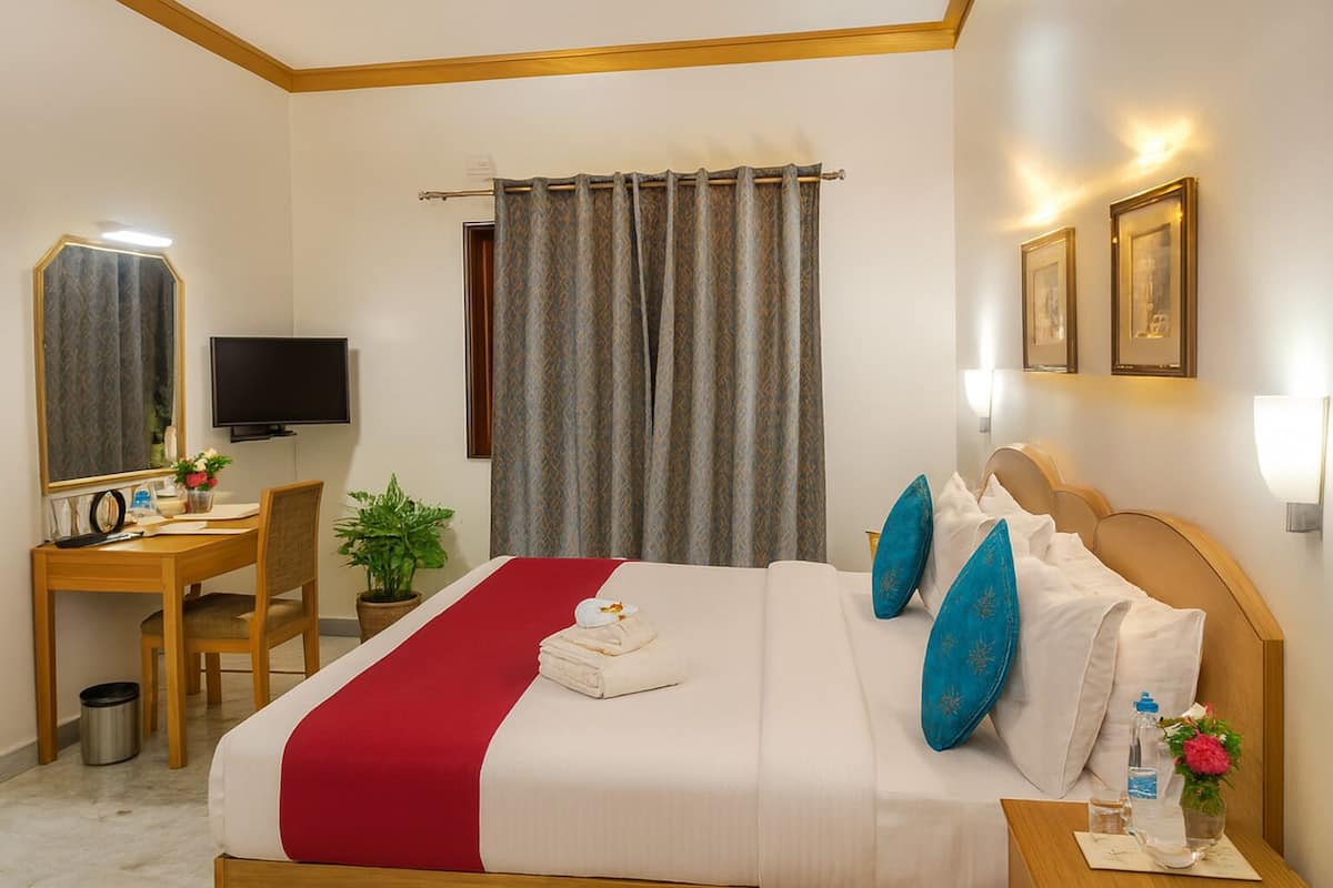 Habitación de hotel con cama, escritorio, silla, televisión y ventana con cortinas.