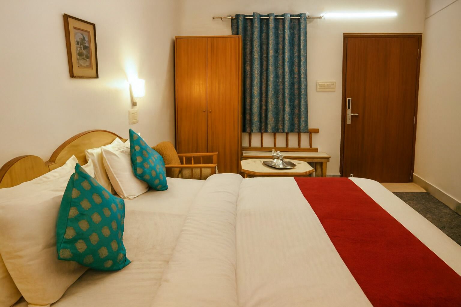 A hotel room with a bed, a small table, a chair, a wardrobe, and a curtain.