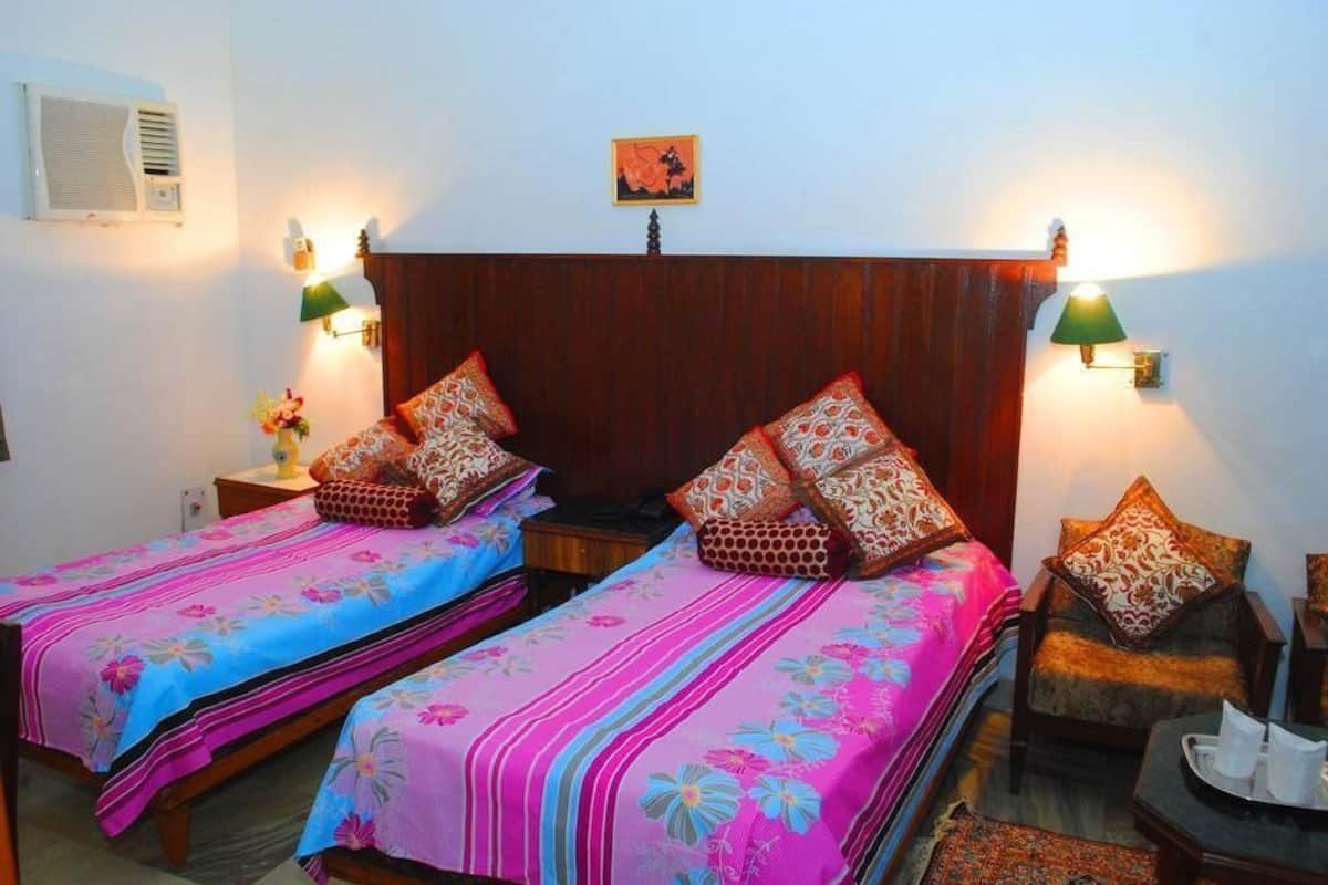Habitación con dos camas, cada una con cubrecamas florales y almohadones estampados, cabeceras de madera, lámparas de pared y una mesita con bandeja.