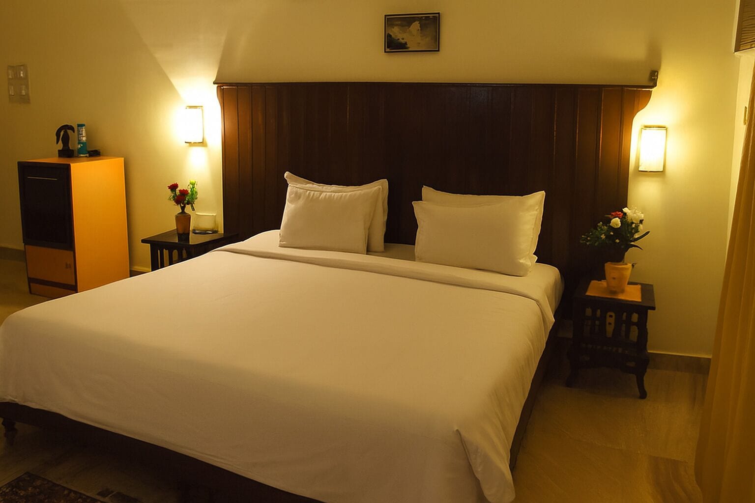 A hotel room with a large bed, two bedside tables with lamps, a dresser, and a framed picture on the wall.
