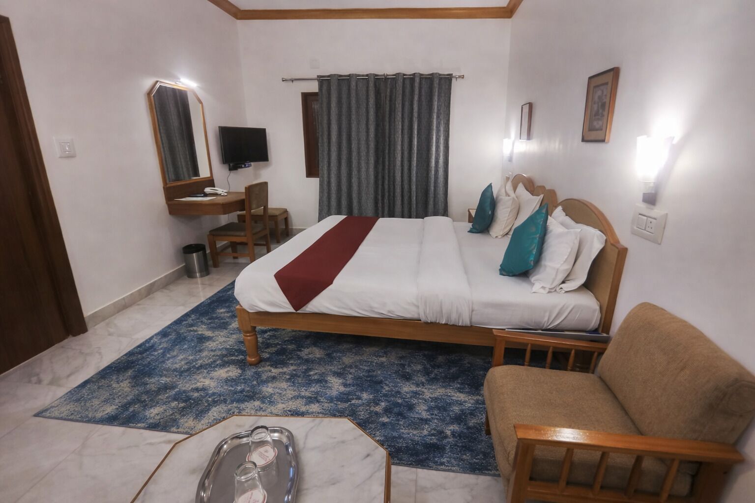 A hotel room with a bed, a desk, a chair, a TV, and a bathroom.