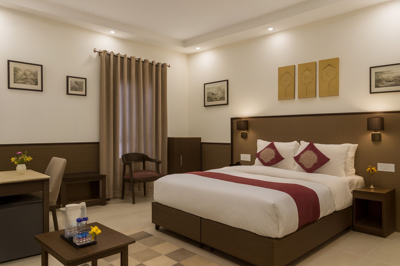 A hotel room with a large bed, a desk, a chair, and a small table with a vase of flowers.