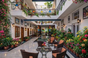 Un vaste atrium intérieur doté d’une table en verre au centre, entourée de fauteuils en osier, et agrémenté de plantes et de fleurs en pot.
