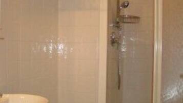 Un baño con ducha, dos lavamanos y un inodoro.
