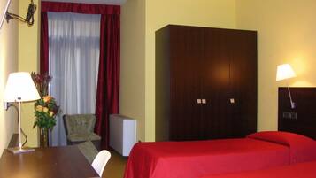 A hotel room with a bed, a desk, a chair, a wardrobe, and a window with curtains.
