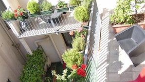 A rooftop garden with potted plants and flowers, a metal railing, and a red chair. - Albergo Verdi (Padova)