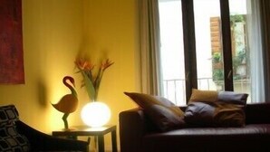 A living room with a sofa, a small table with a lamp, and a vase with flowers. - Albergo Verdi (Padova)