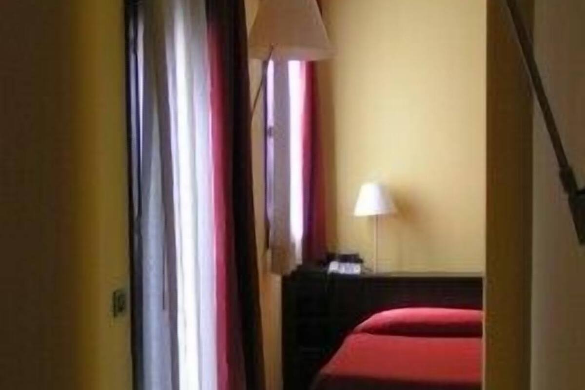 Une chambre d’hôtel avec deux lits, un canapé, une lampe et une fenêtre avec des rideaux.