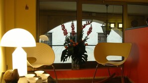 A room with a dining table, two chairs, a lamp, a vase with flowers, and a view of buildings through a window. - Albergo Verdi (Padova)