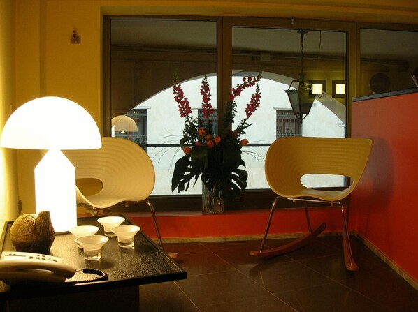 A room with a dining table, two chairs, a lamp, a vase with flowers, and a view of buildings through a window. - Albergo Verdi (Padova)