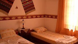A small hotel room with two single beds, a nightstand, a lamp, and a patterned wall hanging. - Duygu Pension (Fethiye)
