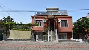 A two-story building with a red facade, a staircase leading to the entrance, and solar panels on the roof. - Duygu Pension (Fethiye)