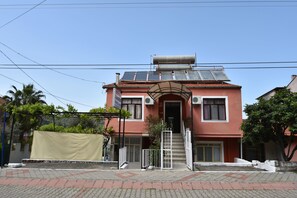 A two-story building with a red facade, a staircase leading to the entrance, and solar panels on the roof. - Duygu Pension (Fethiye)