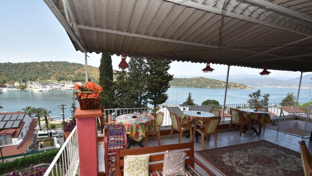 A terrace with outdoor seating, a view of a lake, and boats in the background. - Duygu Pension (Fethiye)